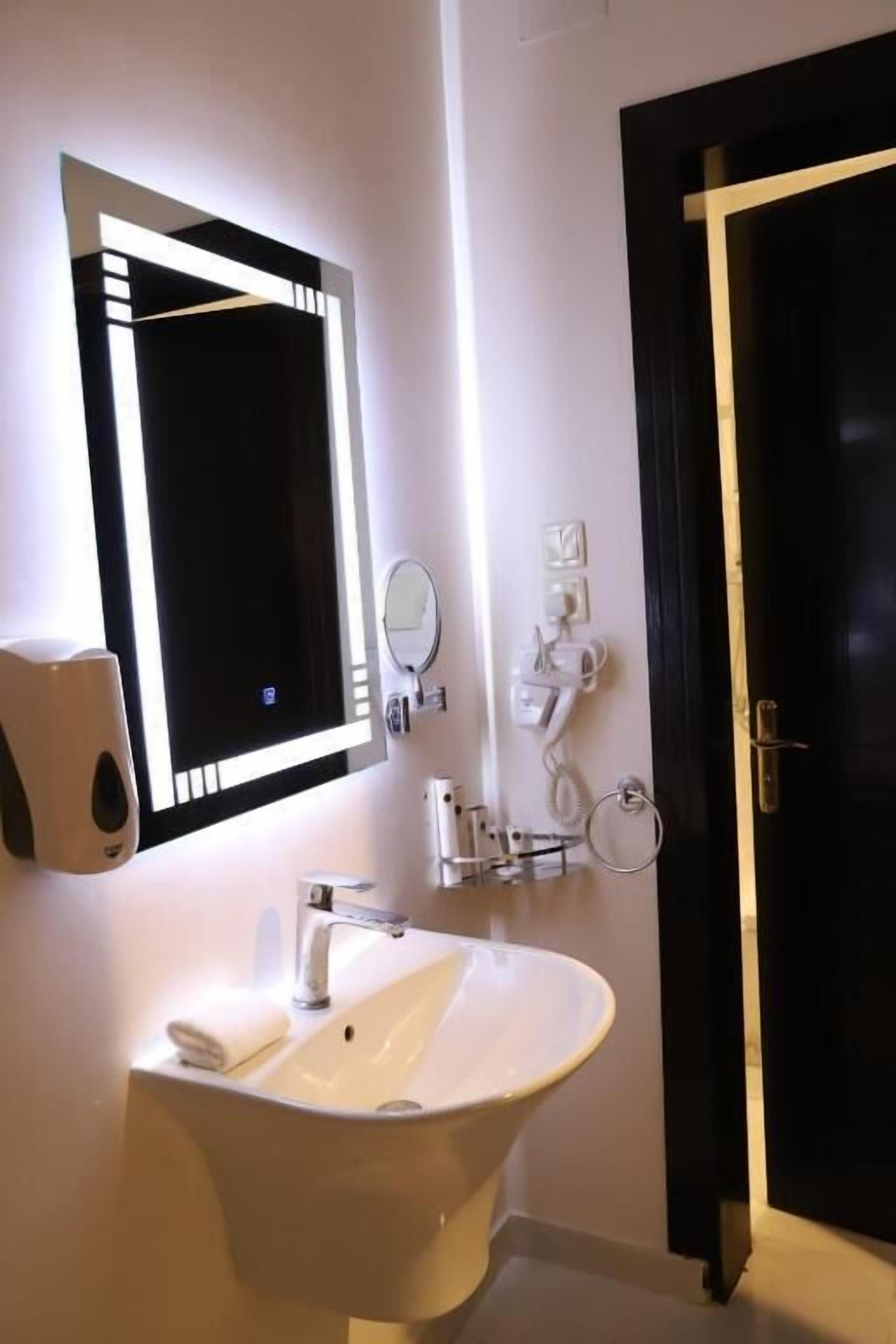Een badkamer met een wastafel, spiegel en handdoekdispenser.