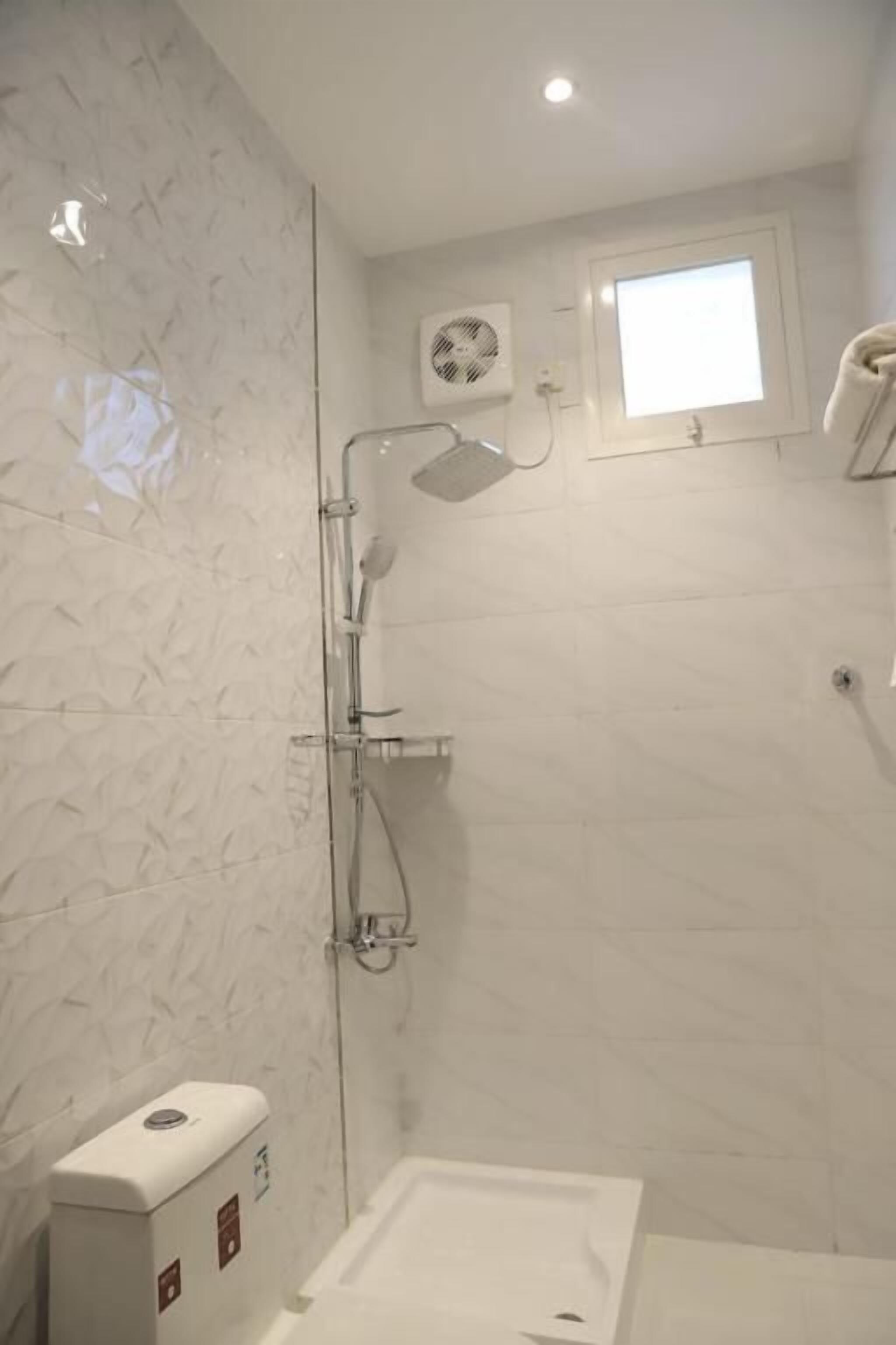 Ein Badezimmer mit Dusche, Toilette und einem kleinen Fenster.