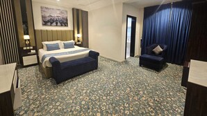 Una habitación de hotel con cama, un banco, una silla, un escritorio y un ventanal grande.