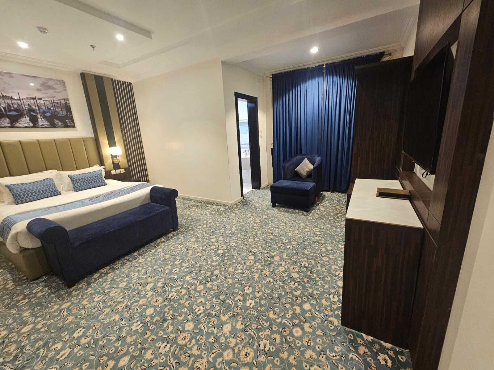 Habitación de hotel con cama, una silla, un escritorio y un amplio ventanal con cortinas.