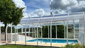 Ein überdachter Pool mit Glasveranda, umgeben von Rasenflächen und Bäumen.