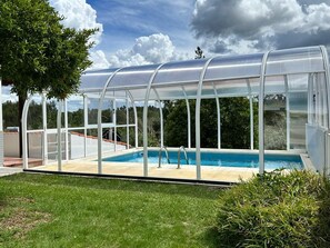 A covered swimming pool with a glass enclosure, surrounded by a grassy area and trees. - Casa Jone | olive tree
__ A country retreat with signature design (poço redondo, junceira, TOMAR)