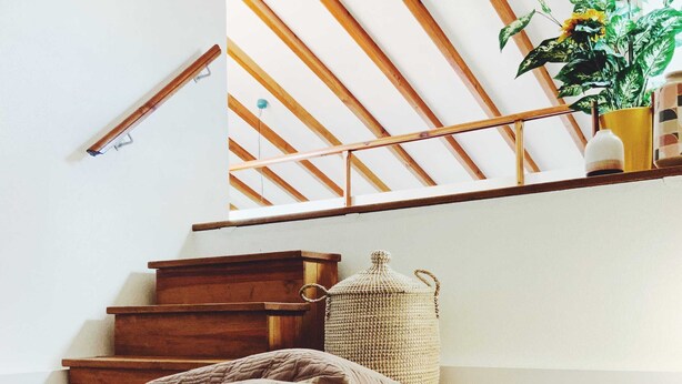 Ein Schlafzimmer mit Bett, Kissen, einem Bücherregal, einer Pflanze und einer Treppe mit Holzbalken.