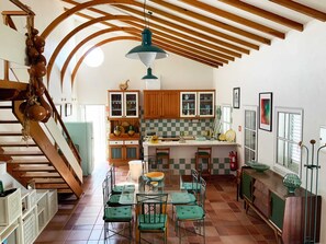 A spacious kitchen with wooden beams, a dining area with green chairs, and a staircase. - Casa Jone | olive tree
__ A country retreat with signature design (poço redondo, junceira, TOMAR)
