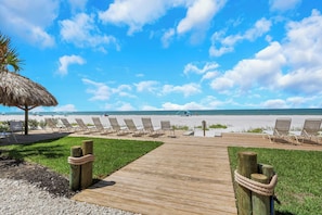 Una passerella di legno conduce a sedie da spiaggia e un ombrellone di paglia, con vista libera sull'oceano.