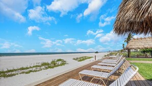 A beachside deck with lounge chairs and a thatched roof structure. - Paradise Beach Getaway  Steps to Sand & Gulf Views  King Bed + Sofa Bed (Fort Myers Beach)