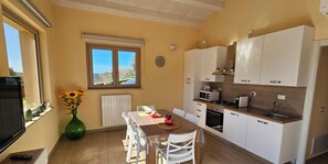 Eine kompakte Küche mit weißen Schränken, einem Esstisch mit Stühlen, einem großen Fenster mit Aussicht und einer Vase mit Sonnenblumen.