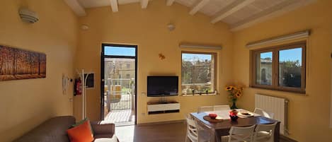 Una sala de estar con sofá, televisor, una mesa de comedor con sillas y ventana con vistas al exterior.