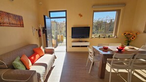 Sala de estar com sofá, televisão, mesa de jantar, cadeiras e janela com vista.