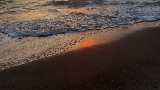 Ein Strand mit Wellen, einem Sonnenuntergang und wolkenlosem Himmel.
