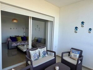 Ein Zimmer mit einer Schiebeglastür, die auf einen Balkon führt, Korbmöbeln und dekorativen Wandbildern.