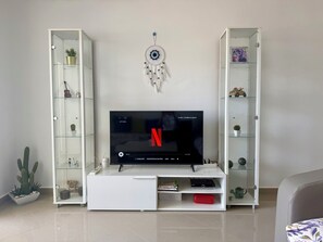 Ein Wohnzimmer mit Flachbildfernseher auf einer weißen Unterhaltungseinheit, umgeben von raumhohen Schränken mit Glastüren und verschiedenen Dekorationselementen.