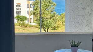 A balcony with a view of the sea, a chair, a small table with a plant, and a building in the background. - Magnificent sea & golf views. Pools, Terraces (Asilah)