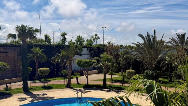 A swimming pool surrounded by palm trees and greenery, with a clear sky above. - Magnificent sea & golf views. Pools, Terraces (Asilah)