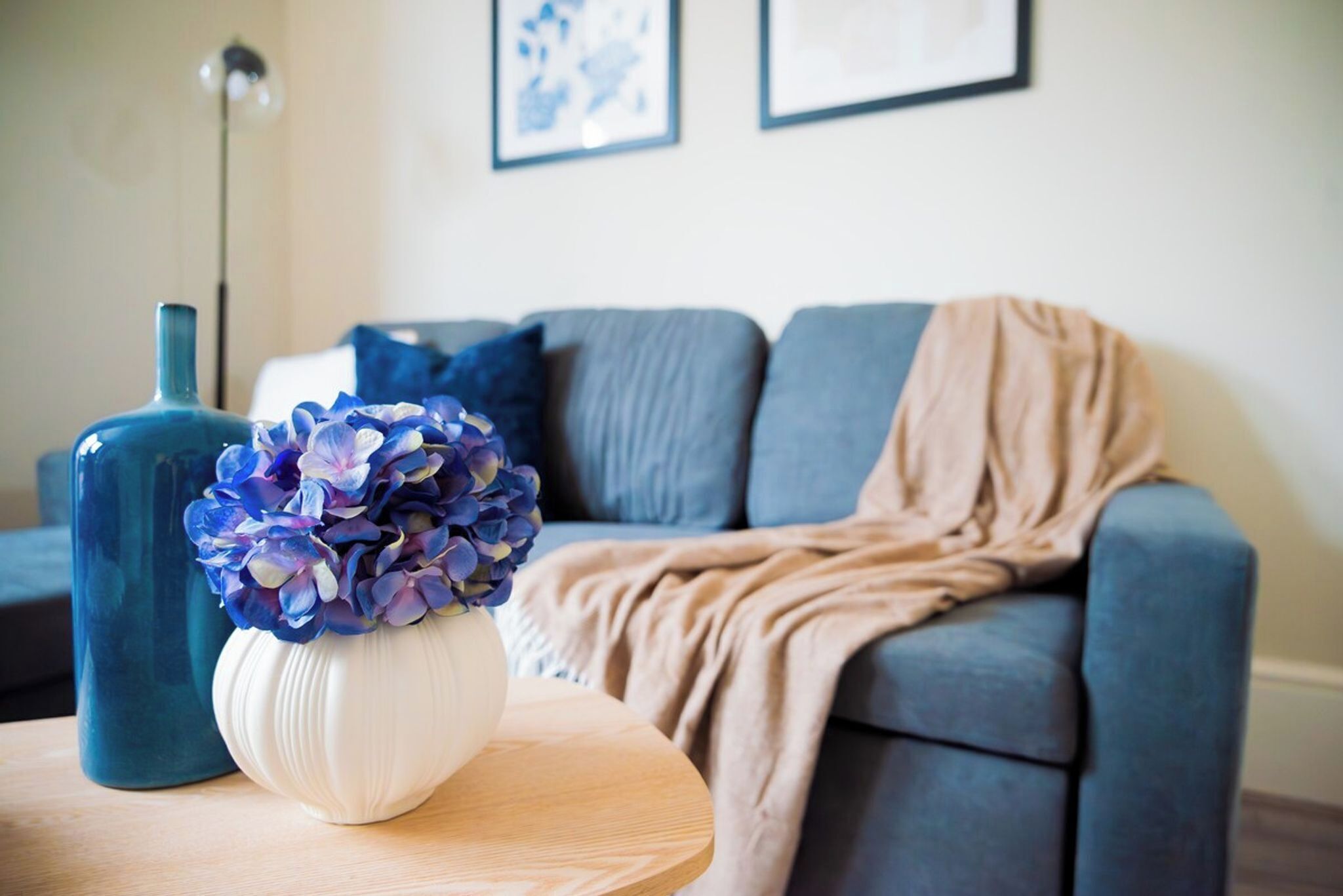 Una sala de estar con un sofá, una mesa redonda de madera y un jarrón con flores.
