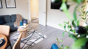 Een woonkamer met een bank, een salontafel, een vloerkleed en een televisie aan de muur.