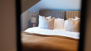 Een net opgemaakt bed met kussens en een hoofdbord, een bedlampje en een behang met een patroon.