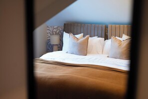 Ein ordentlich bezogenes Bett mit Kissen und Kopfteil, eine Nachttischlampe und eine Wand mit Muster.
