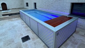 Ein rechteckiger Pool mit Holzdeckrand, umgeben von Steinmauern und einem Steinboden.