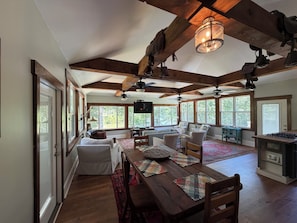 Amplia sala de estar con techo alto, vigas de madera, una mesa de comedor con sillas y ventanas grandes que ofrecen vistas al exterior.