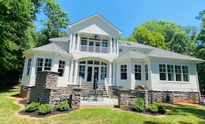 A two-story house with a balcony, stone foundation, and a front porch with outdoor furniture.