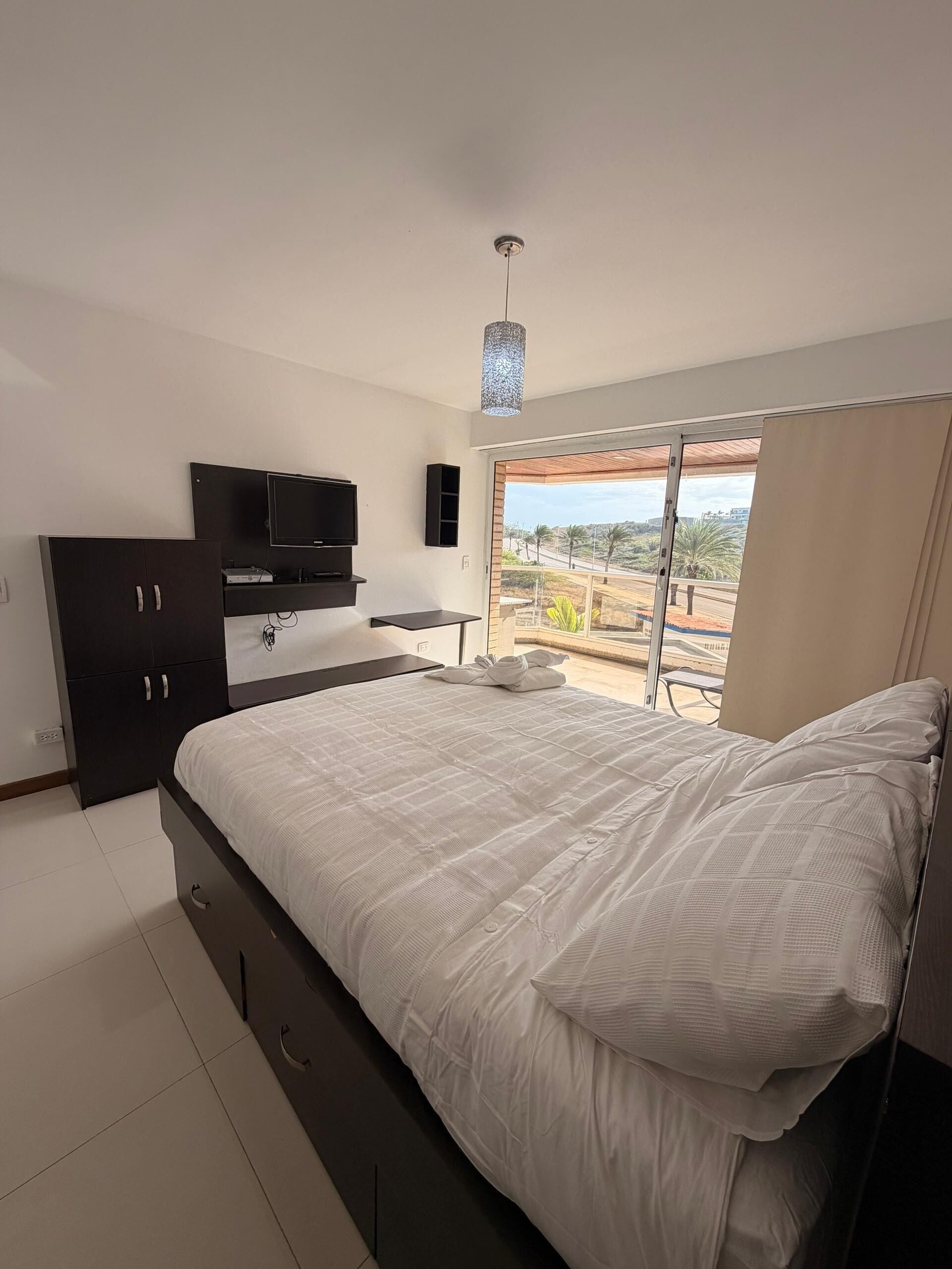 Quarto com cama, televisão, guarda-roupa e vista para o exterior.