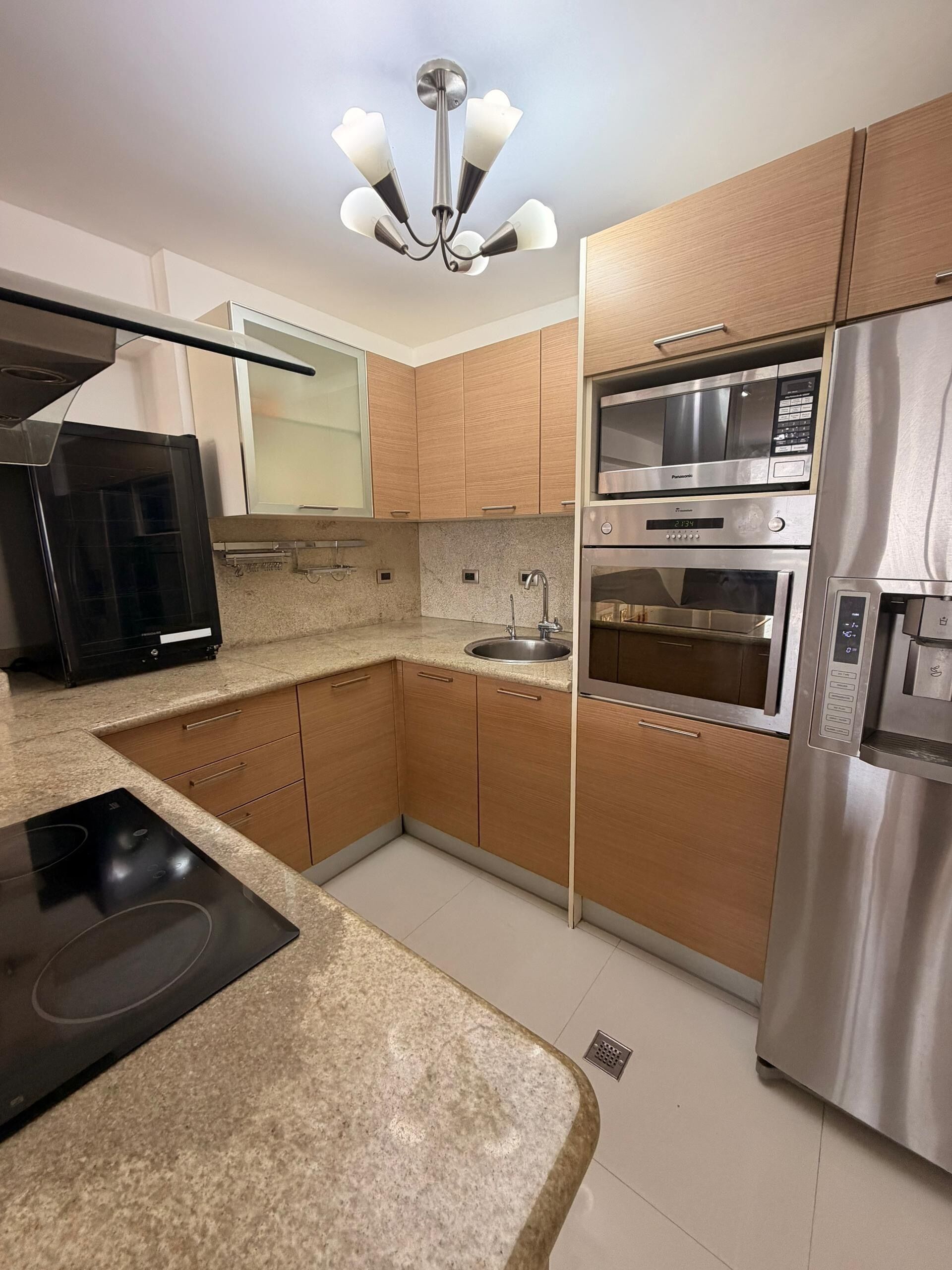 A modern kitchen with wooden cabinets, a stainless steel refrigerator, a built-in oven, a microwave, and a gas stove.