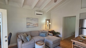 En stue med sofa, lampe, et maleri og et køkken med et køleskab.