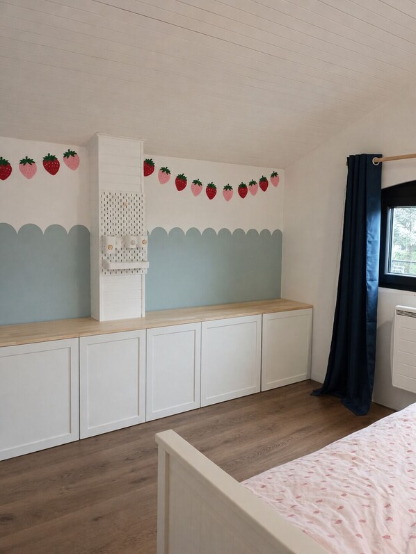 Une chambre à coucher avec un lit, une fenêtre avec un rideau, une étagère fixée au mur et une décoration murale représentant des fraises.