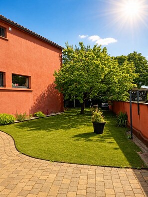 A well-maintained lawn, a large tree, and a building with a red exterior. - Air-conditioned villa 150 m2, heated pool, pétanque, terrace with pergola! (Saint-Paul-Trois-Châteaux)