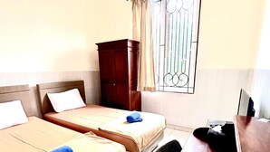 A hotel room with two beds, a desk, a chair, and a window with bars.