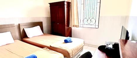 Camera d'albergo con due letti, una scrivania, una sedia e una finestra con grate.