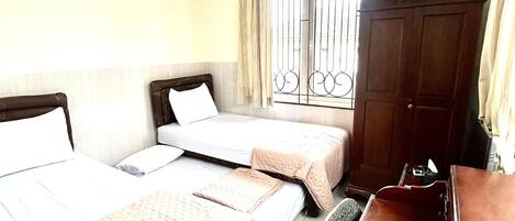 A hotel room with two beds, a desk, a wardrobe, and a window with metal bars.