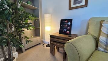 Una habitación con una planta en maceta, un cartel enmarcado de una guitarra, una lámpara y una silla.