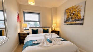 A hotel room with a bed, two bedside lamps, a window with blinds, a painting on the wall, and a mirror. - Character Bedford Apartment With Two Bedrooms (Bedford)