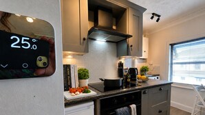 A modern kitchen with a digital thermometer, a stove, a sink, and a window with blinds. - Character Bedford Apartment With Two Bedrooms (Bedford)