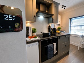 A modern kitchen with a digital thermometer, a stove, a sink, and a window with blinds. - Character Bedford Apartment With Two Bedrooms (Bedford)