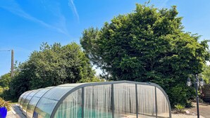 En genomskinlig växthuskonstruktion med ett välvt tak, omgiven av träd och en klar himmel.