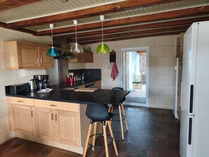 A kitchen with wooden cabinets, a black countertop, a coffee maker, and a refrigerator. - Two gîtes in the countryside for 25 people: indoor swimming pool and play areas (Montrevault-sur-Èvre)