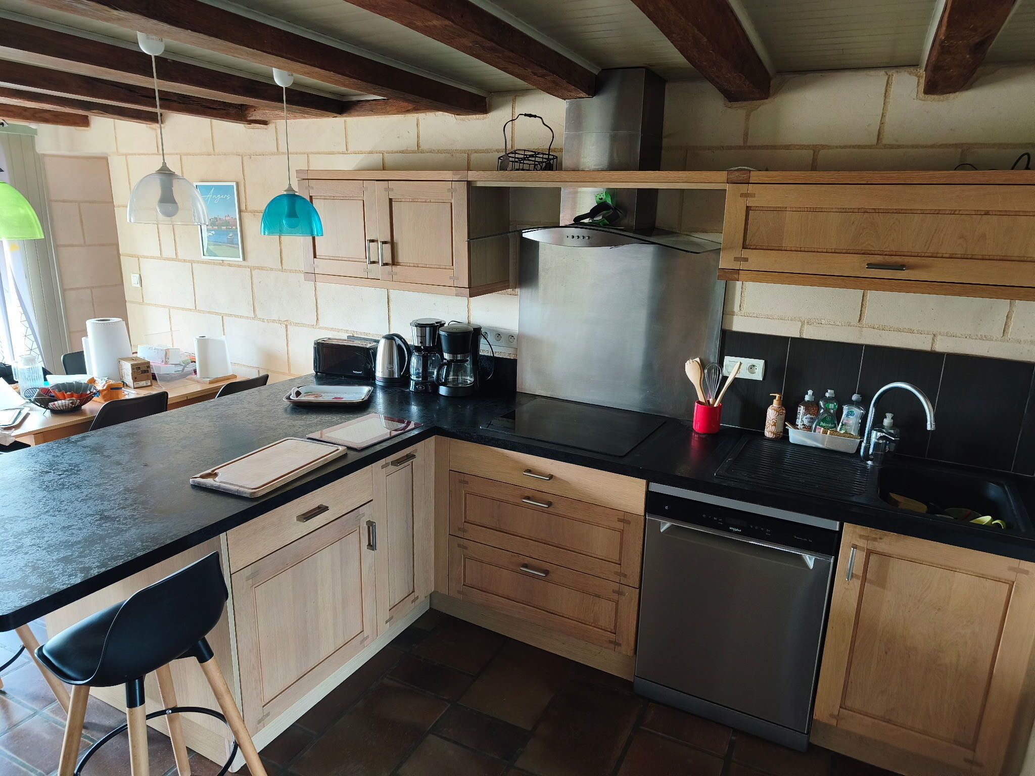 A kitchen with wooden cabinets, a black countertop, a stainless steel dishwasher, and a hanging light fixture.