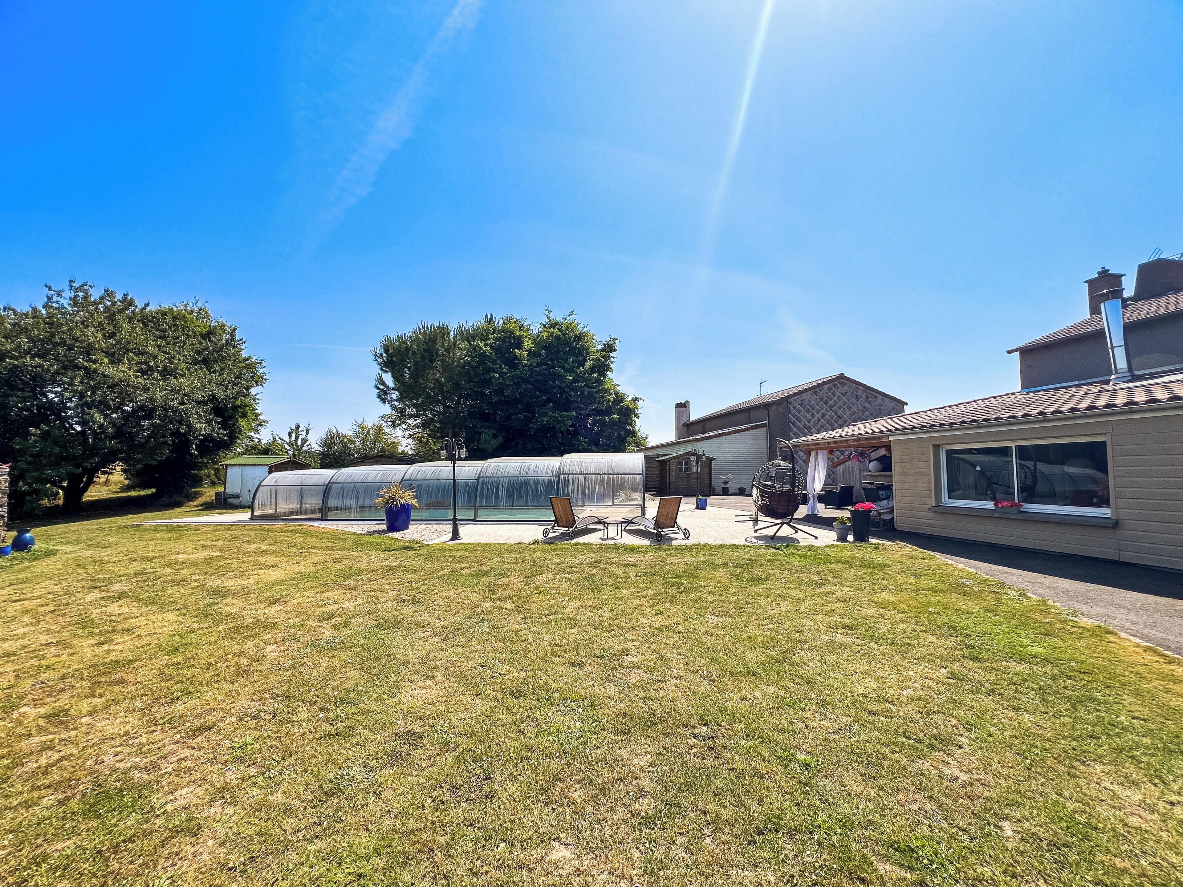 Una casa con un invernadero grande de vidrio, un patio con mobiliario exterior y un cielo azul despejado.