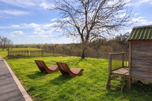 A grassy outdoor area with two wooden lounge chairs, a wooden deck, and a fenced garden. - Two gîtes in the countryside for 25 people: indoor swimming pool and play areas (Montrevault-sur-Èvre)