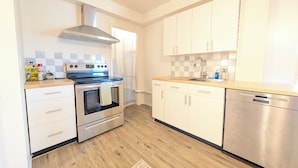 A modern kitchen with stainless steel appliances, white cabinetry, and a wooden floor.