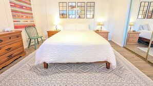 A bedroom with a bed, two bedside tables, a chair, a dresser, a mirror, and a ceiling fan.