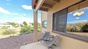 A patio with two chairs and a small table, a large window with a view of the landscape, and a building exterior with a textured wall.