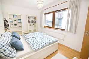 Ein Schlafzimmer mit einem Bett, zwei weißen Bücherregalen, einem Fenster mit Vorhängen und einer Heizung.