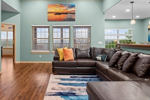 A living room with a sectional sofa, a painting, and a view of the outdoors. - Beautiful remodel, Game Room, Hot Tub, Pools, GOLF (Branson West)