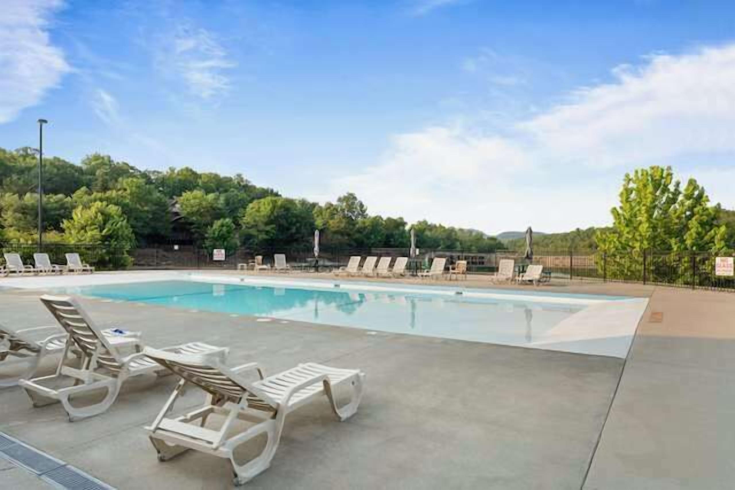 A swimming pool with lounge chairs, surrounded by trees and a clear sky.
