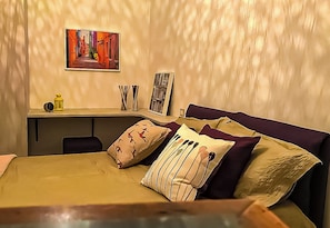 A hotel room with a bed, a desk, a chair, a picture on the wall, and a small table with a lamp and a book. - Cozy Apartment nestled in a fantastic lemon grove. (Maiori)