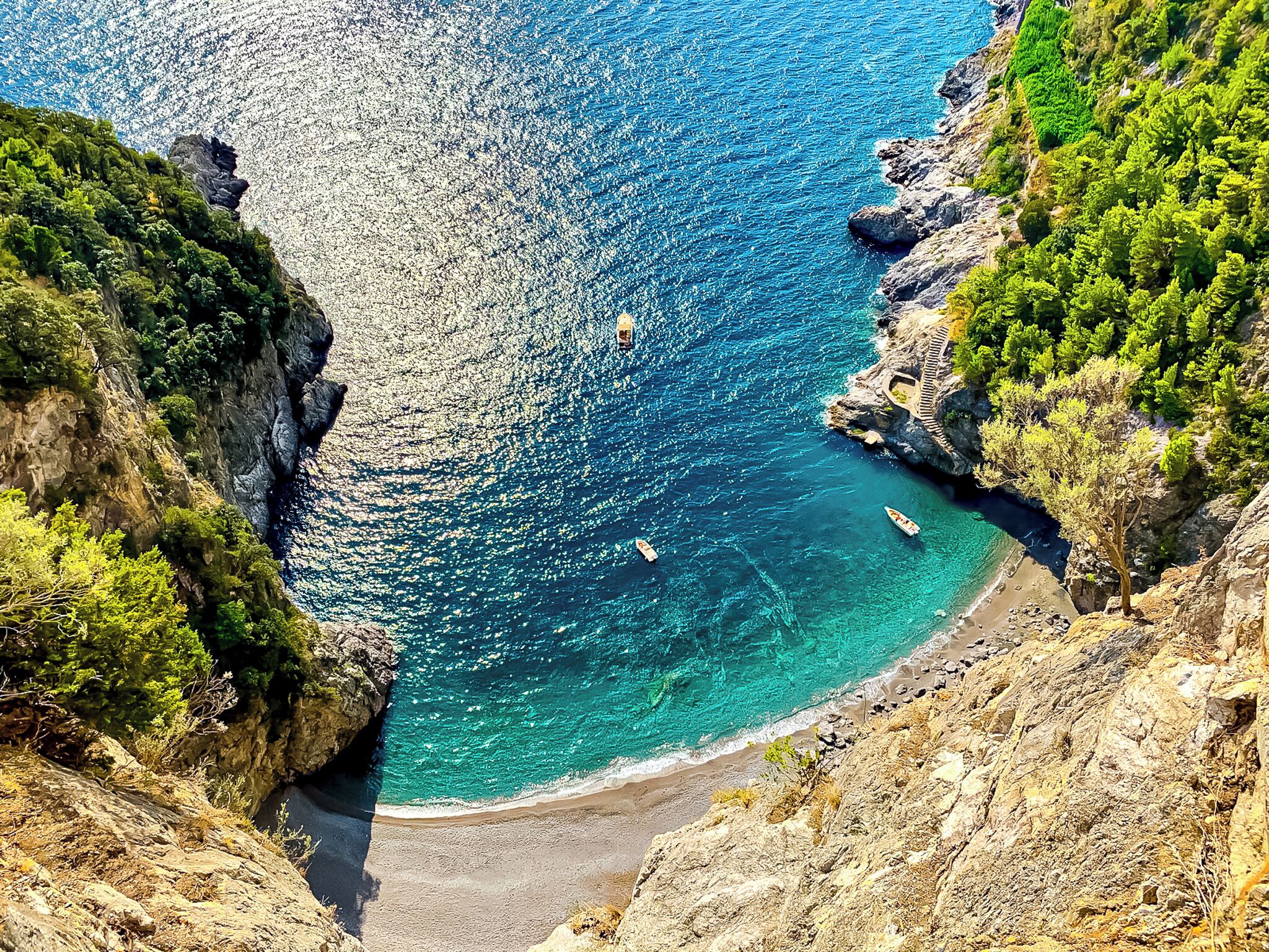 A coastal landscape with rocky cliffs, clear turquoise waters, and a narrow beach.
